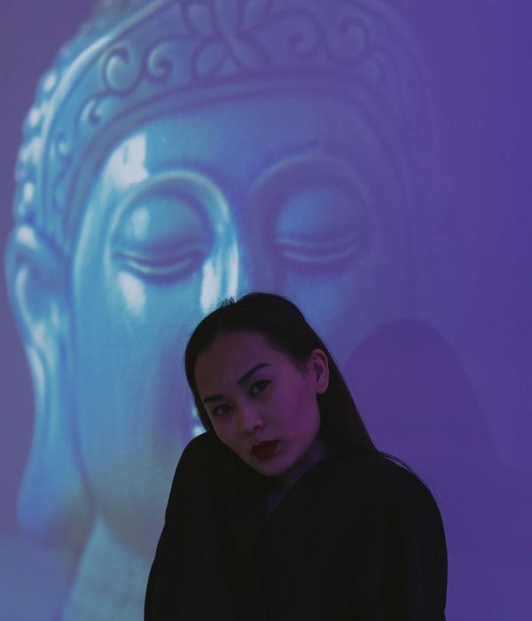 Woman in a calm meditation pose against a dark background with a soft pink light.